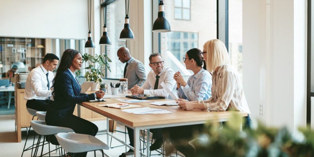Stone Fortress (2) (Medium)_compressed Smiling group of diverse businesspeople discussing paperwork together while having a meeting around a table in a modern office